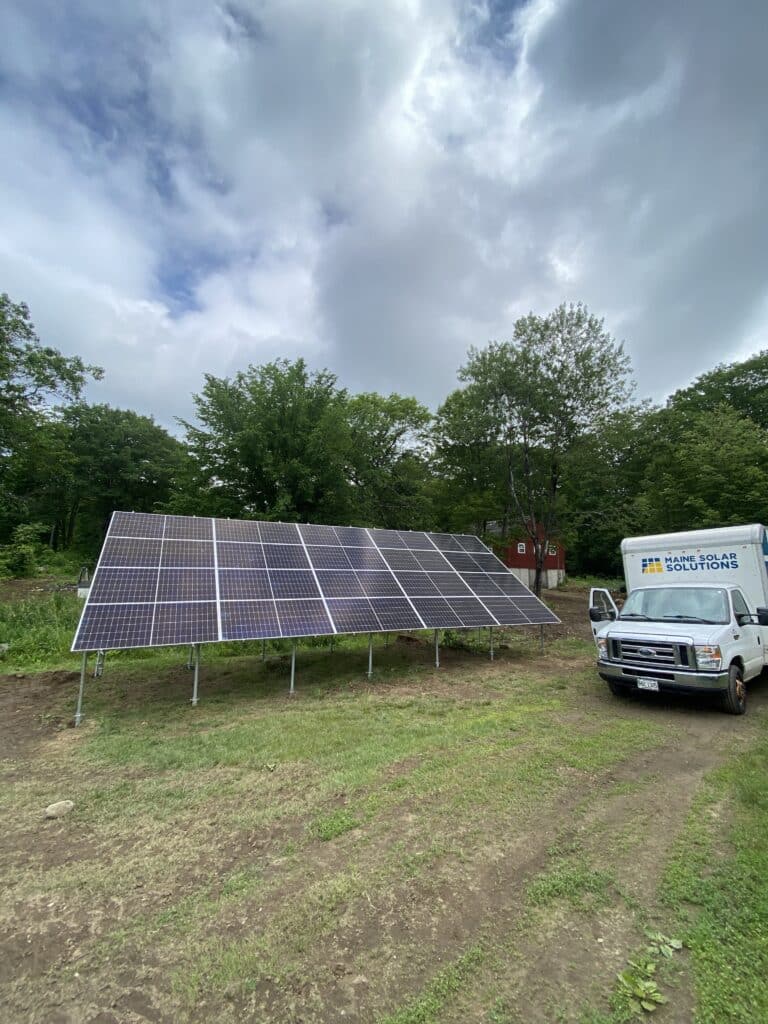 Ground-mounted solar panel system installed by Maine Solar Solutions with company service vehicle on site
